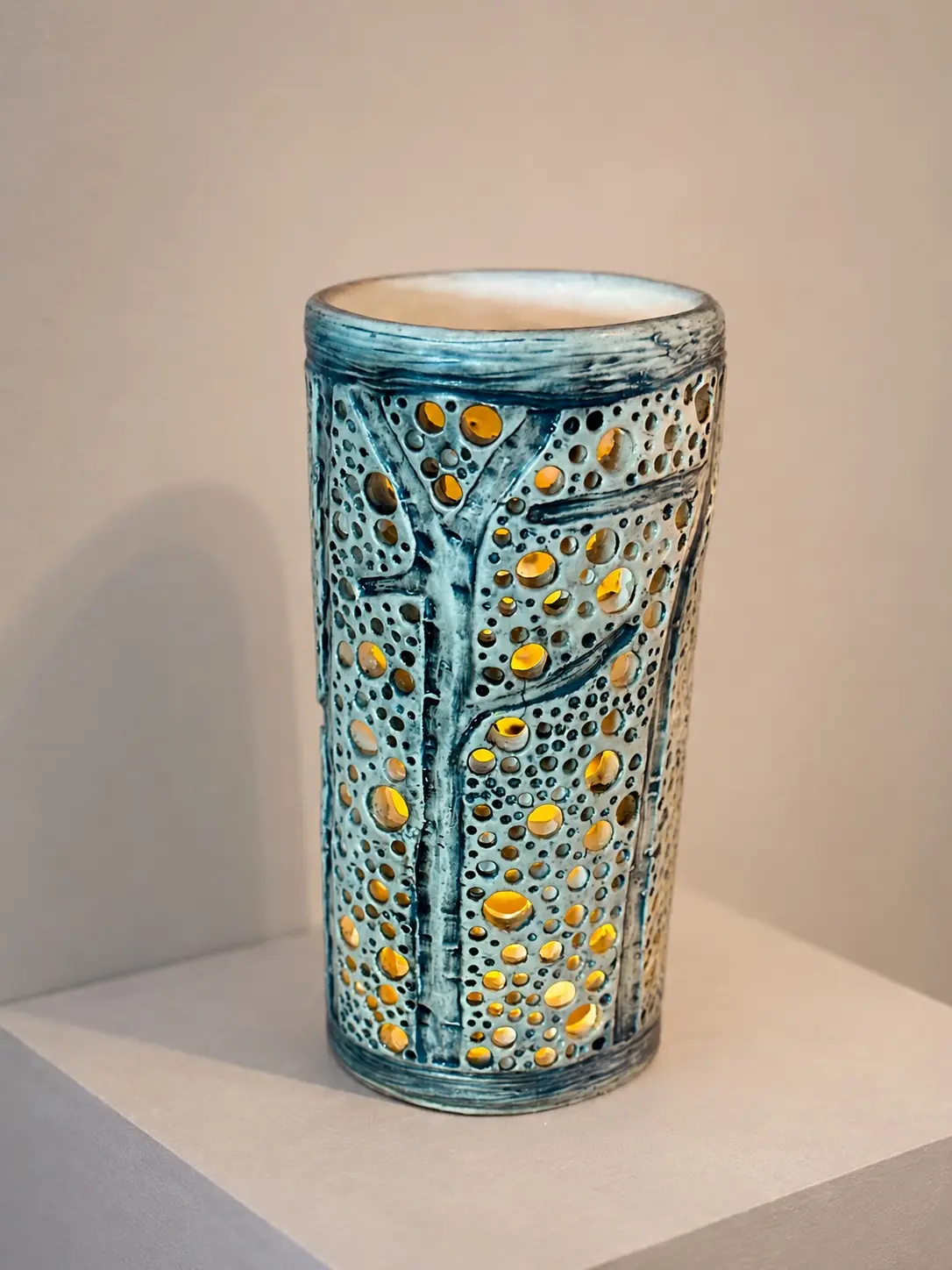 Pierced blue ceramic lantern with branching tree details and a warm glow